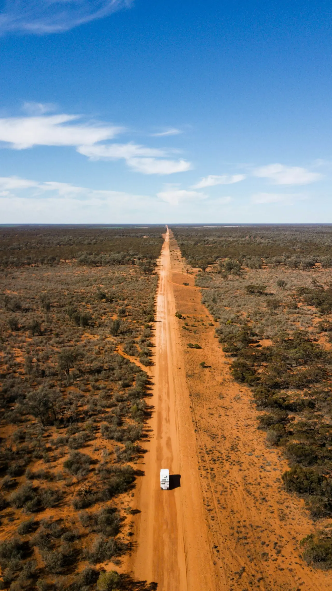 A long red dirt road running straight through scrub to the horizon