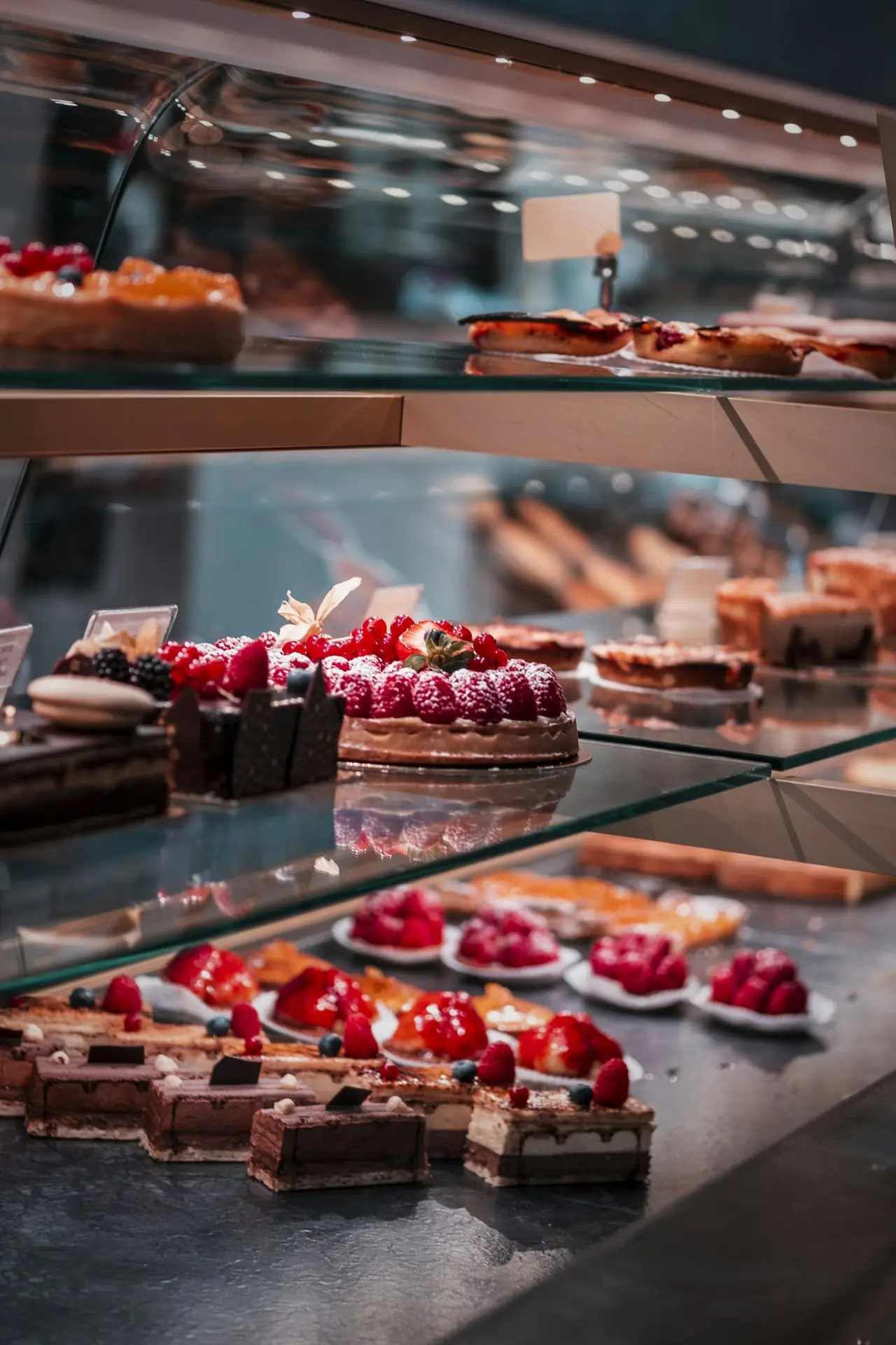 A glass counter full of tarts and cakes topped with berries