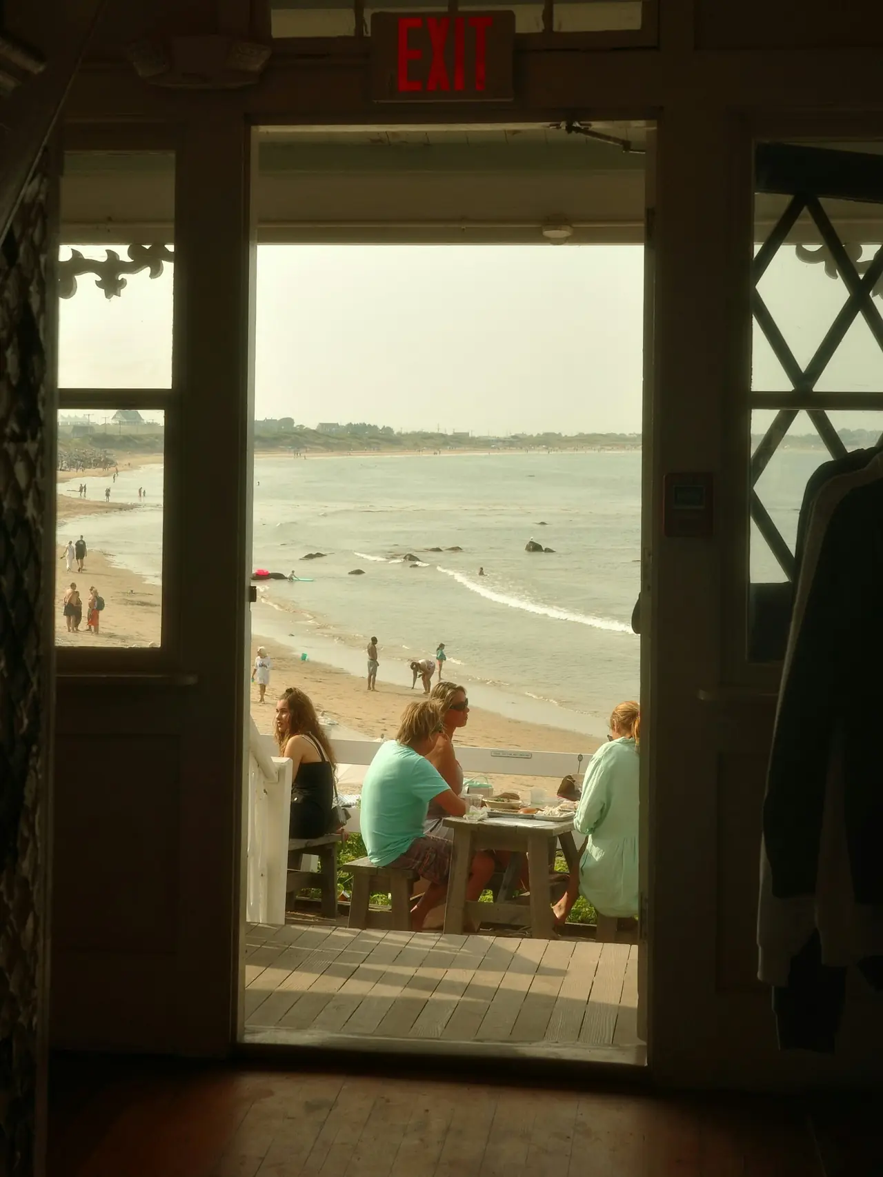 Looking out through an open door to tables on a deck and the beach beyond