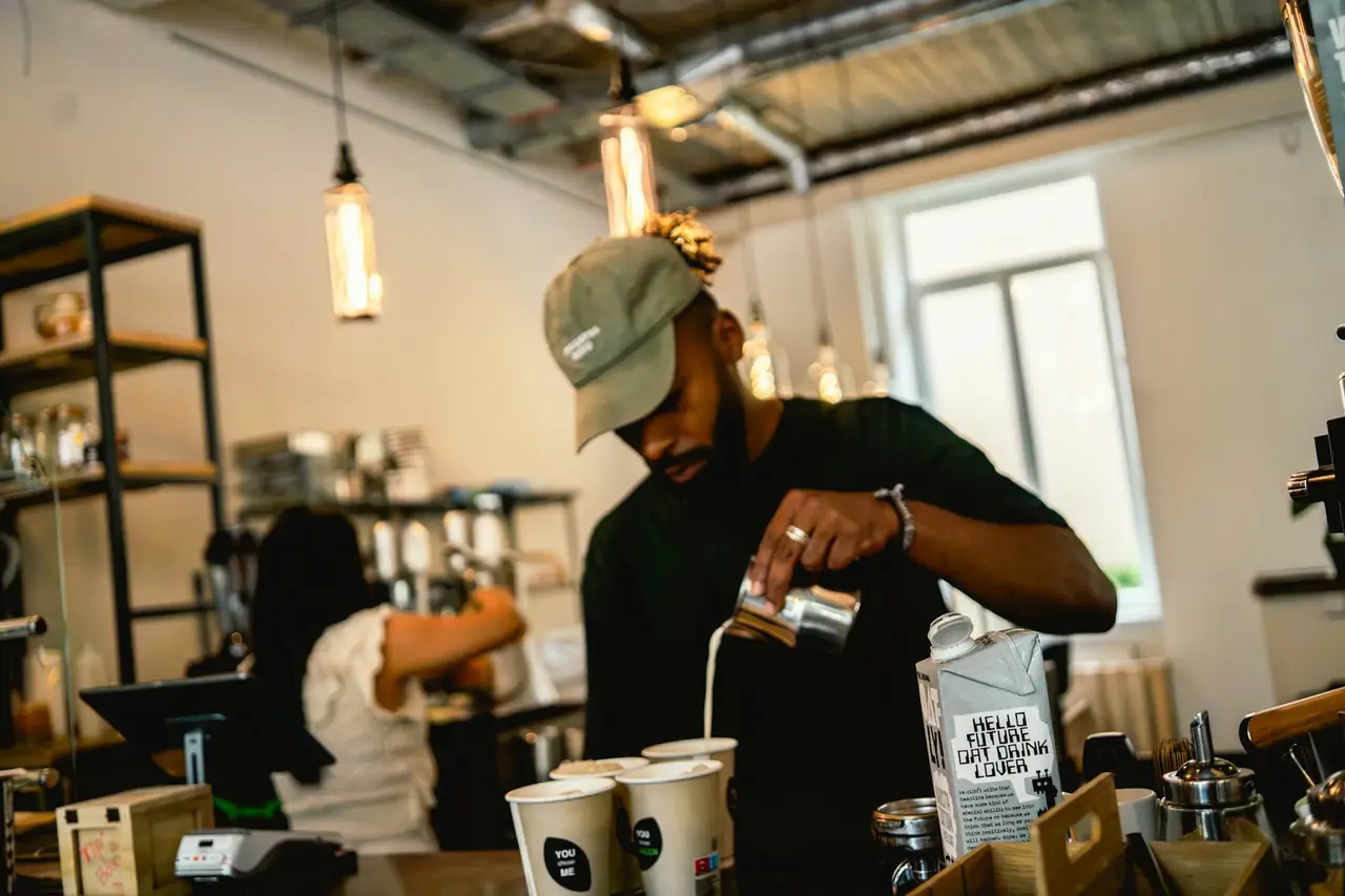 A barista pouring milk into takeaway cups at a bright espresso bar