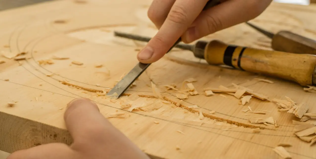 A chisel cutting a carved pattern into a pale timber panel