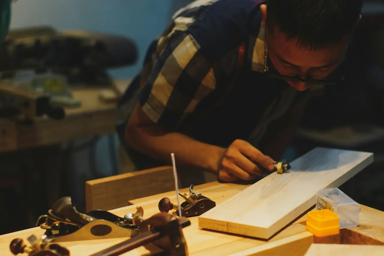 A woodworker in a checked shirt planing a pale board at the bench
