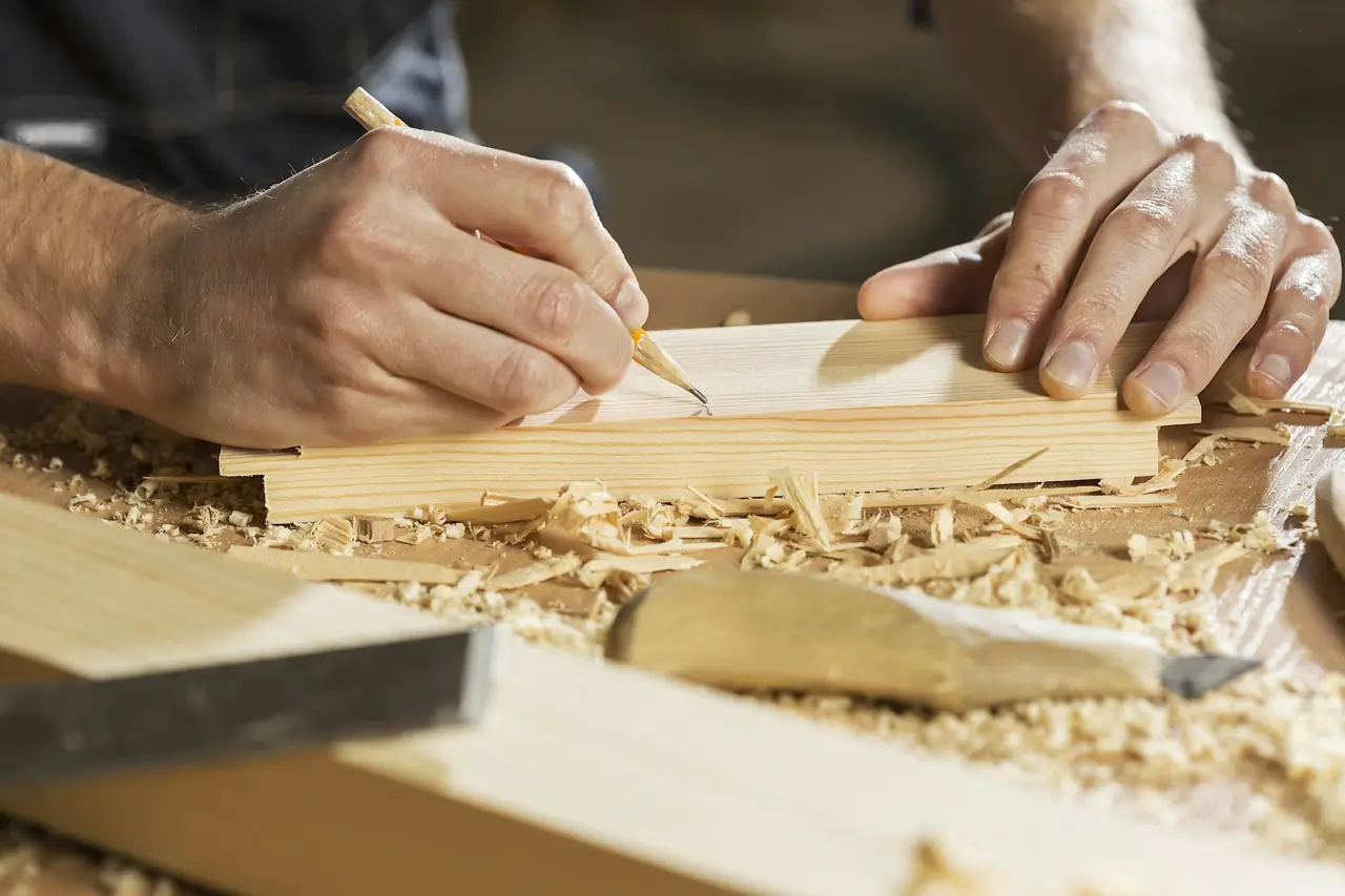 Hands marking a pencil line on a board among wood shavings