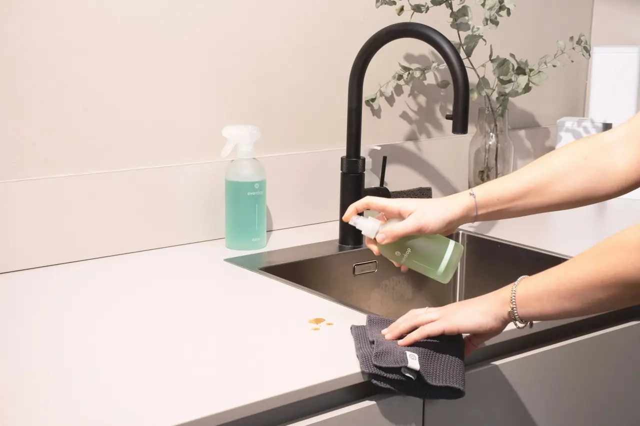 Hands spraying and wiping a black kitchen sink