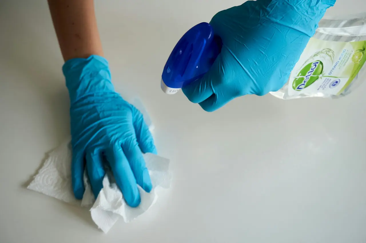 A gloved hand wiping a white surface with a spray bottle