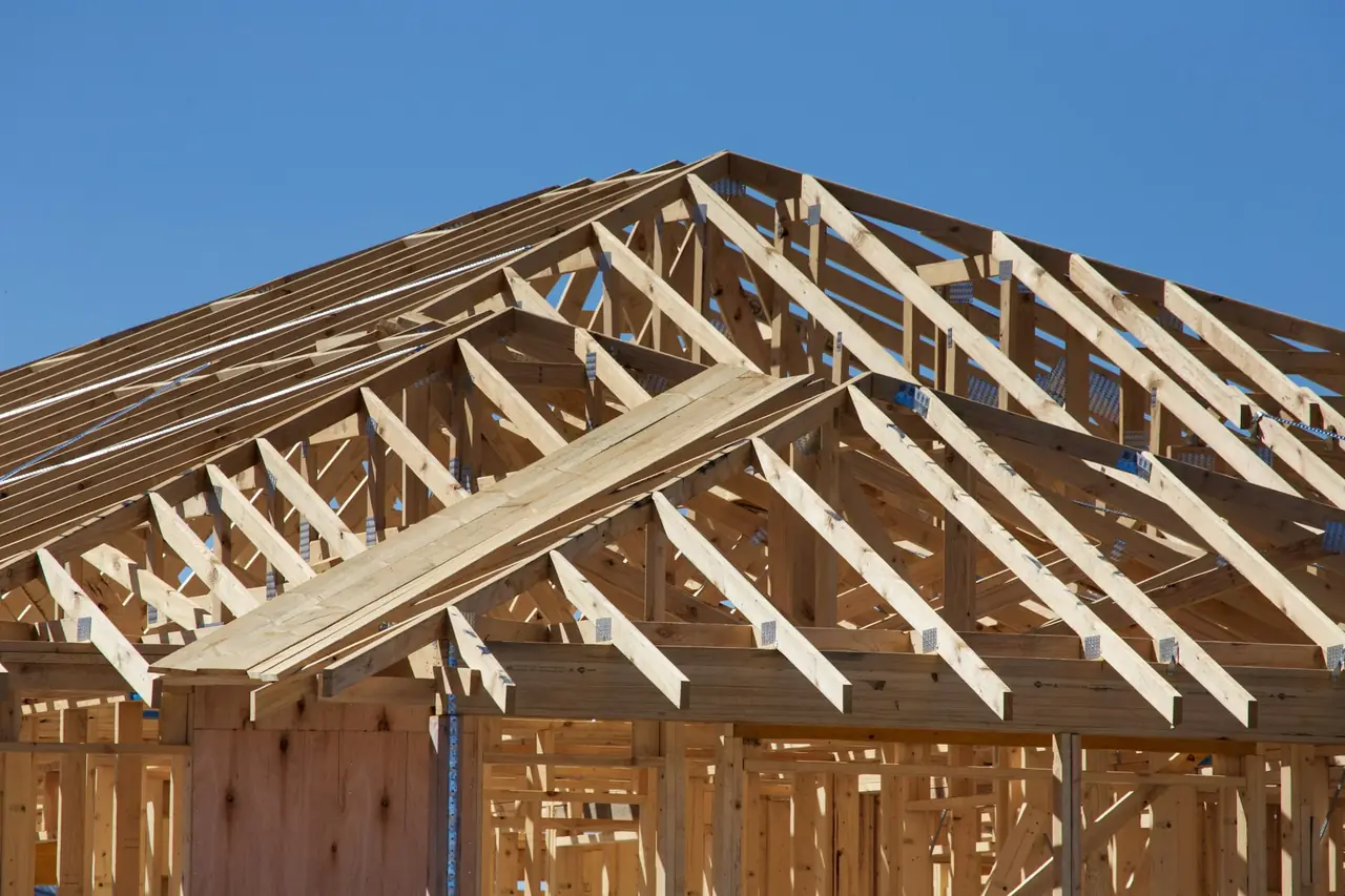A timber roof frame of trusses going up against a blue sky