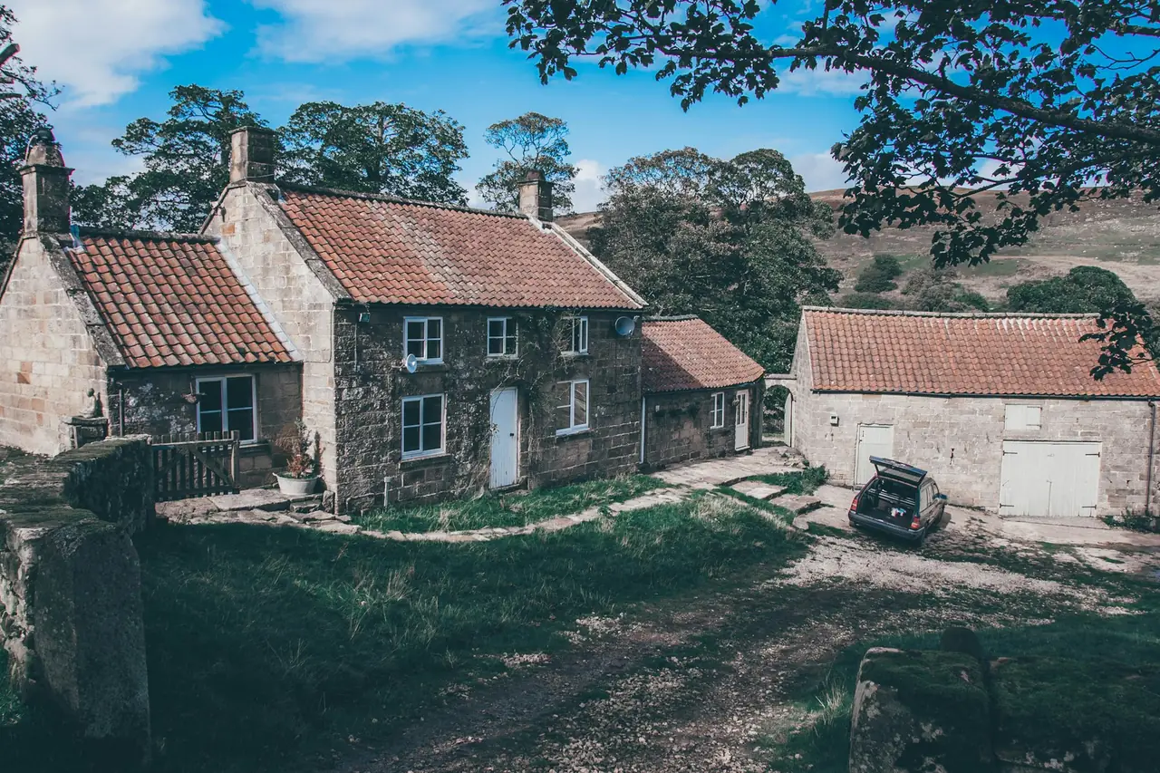 A stone house with a red roof on a sloping, grassy block
