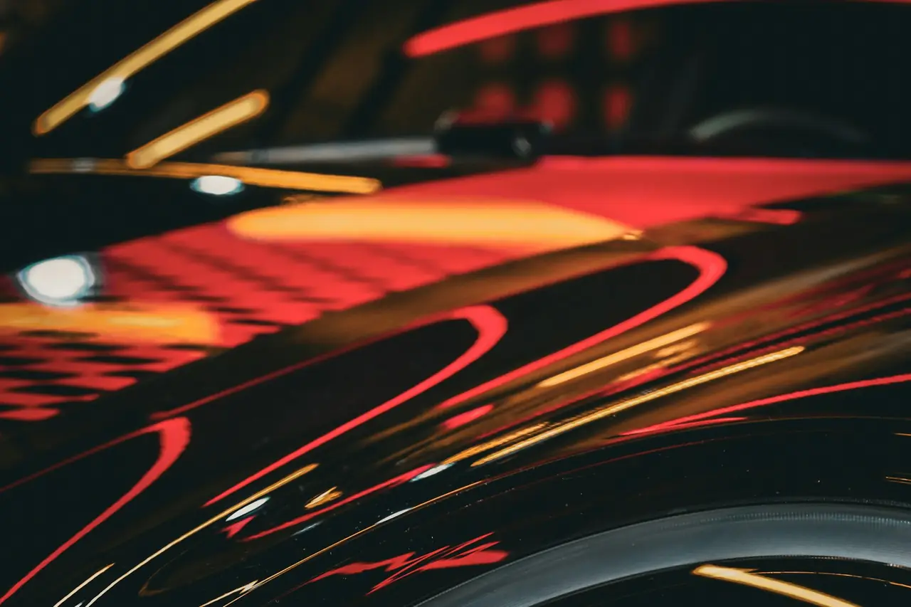 Streaks of red and amber light reflected in glossy car paint