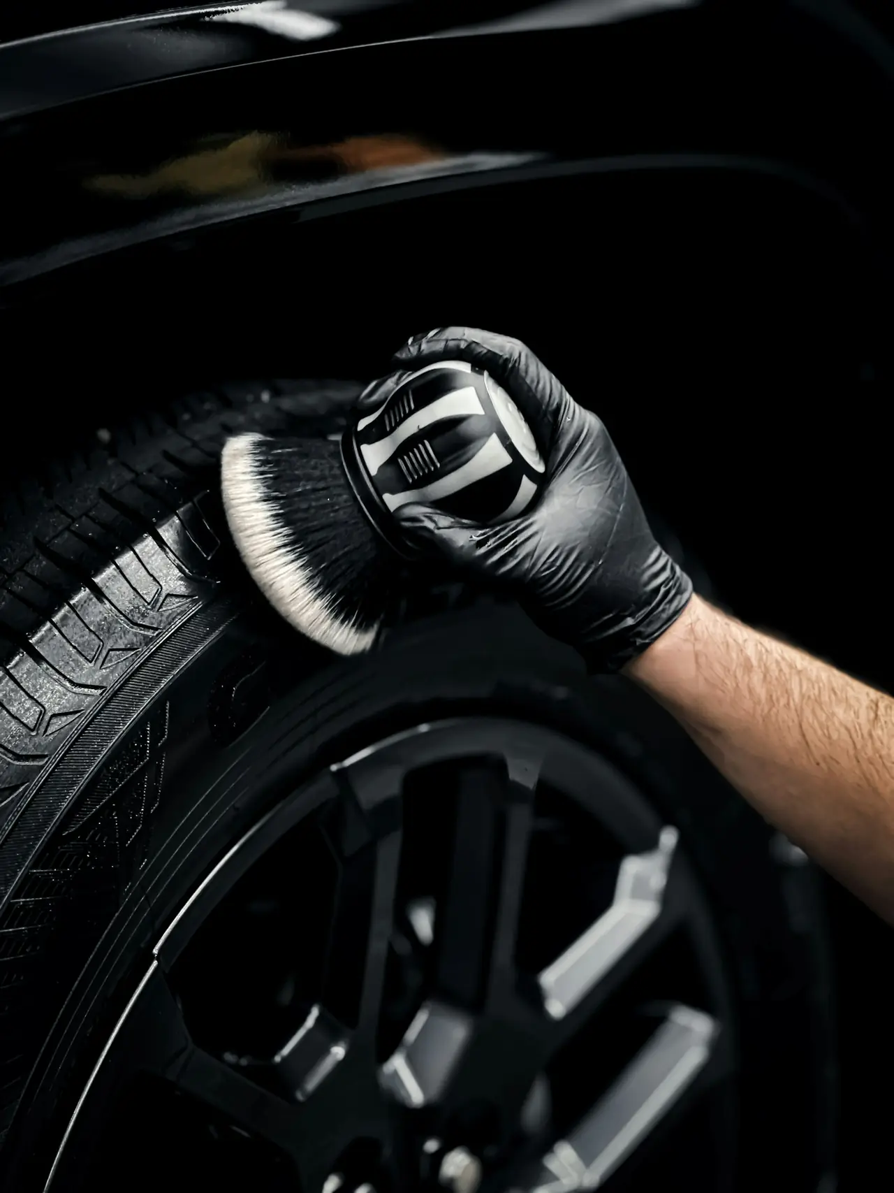 A gloved hand brushing a black alloy wheel