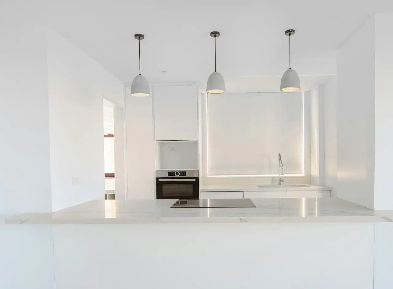 A white kitchen with three pendant lights over the bench