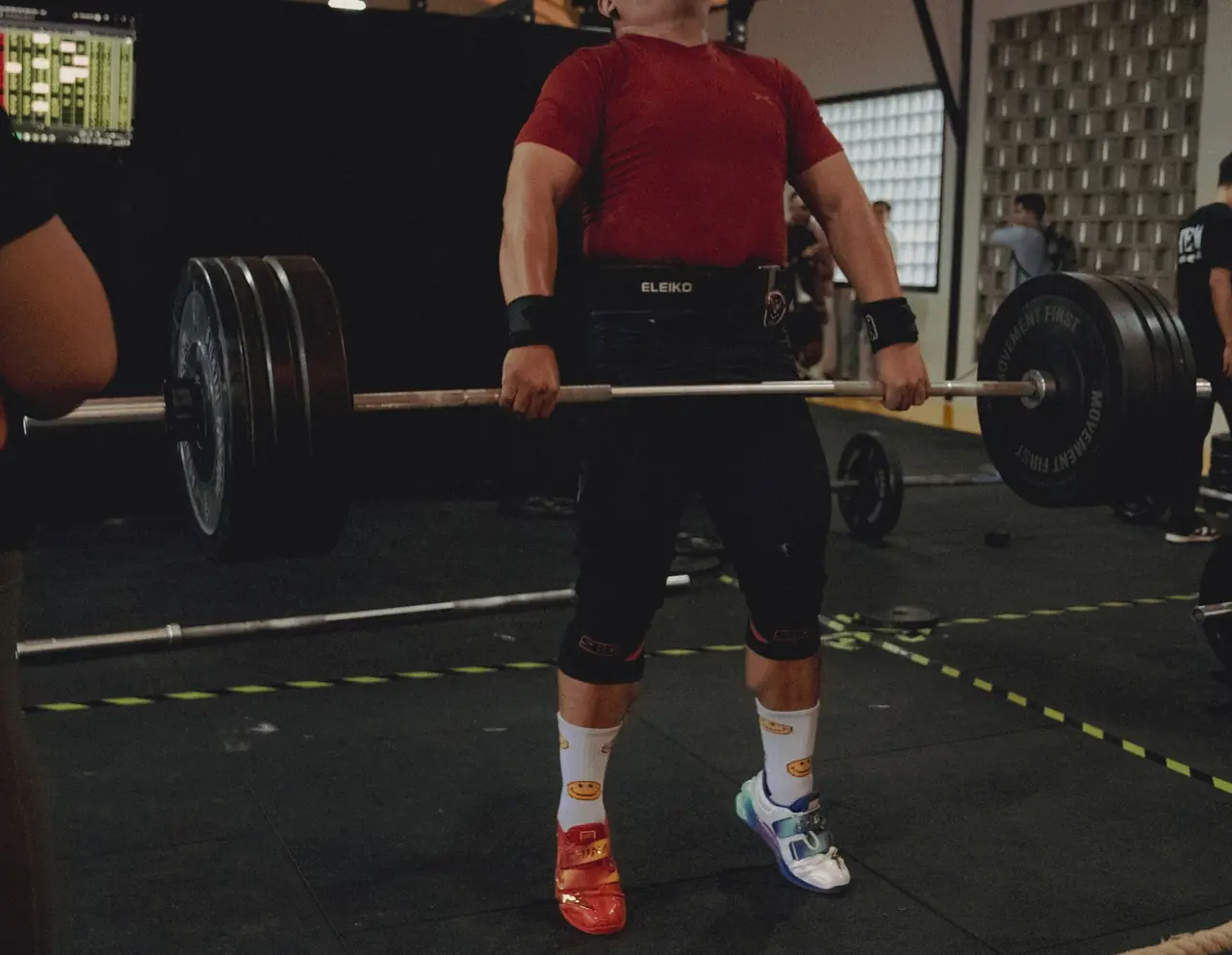 A lifter in a red shirt holding a loaded barbell at the hips