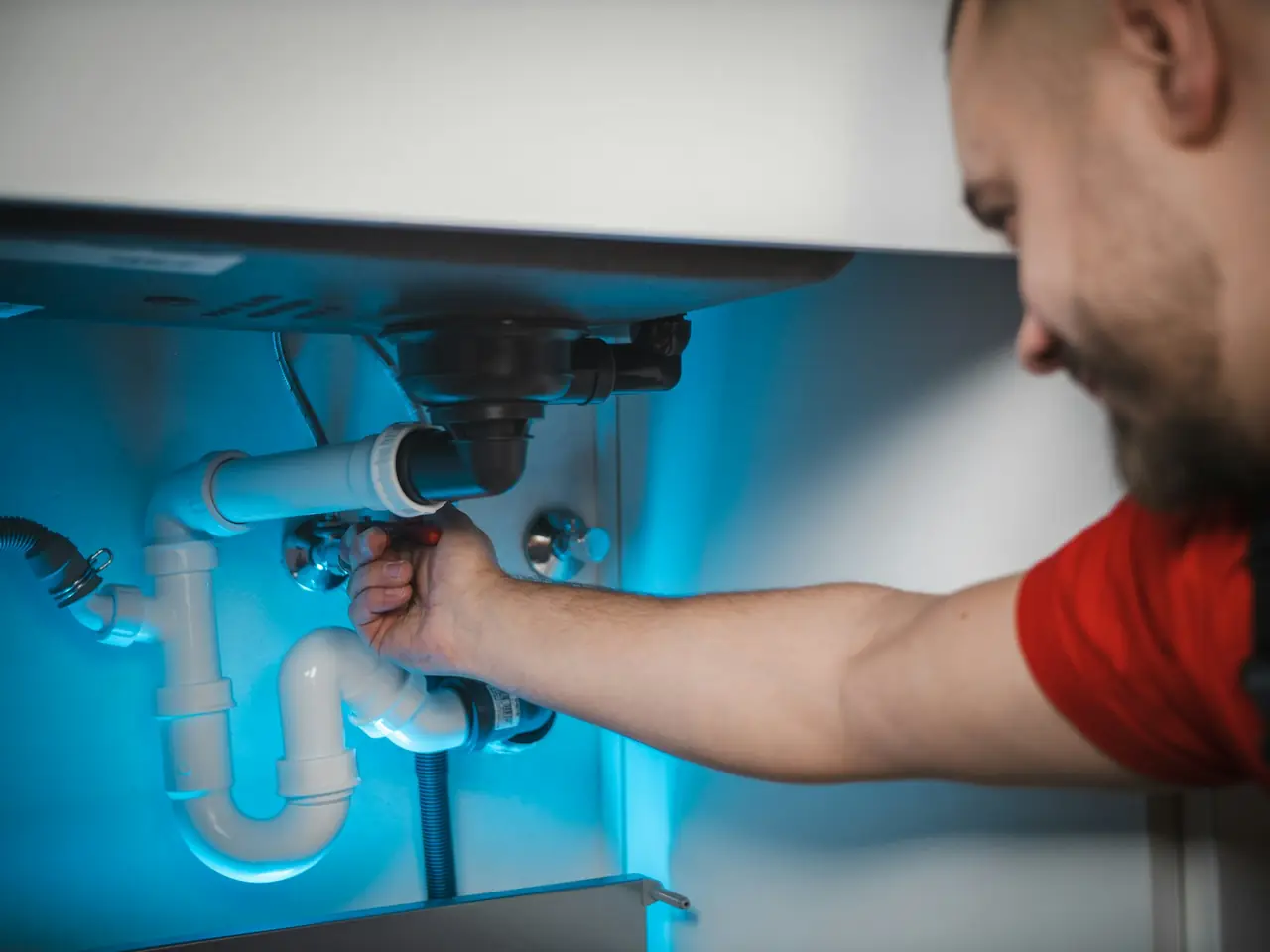 A plumber tightening a waste pipe under a sink