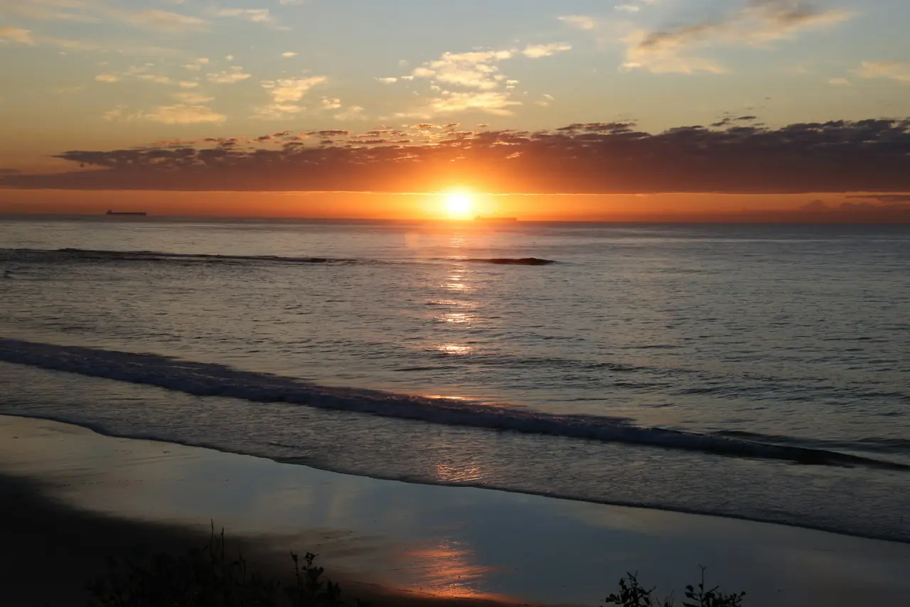 The sun rising over a calm sea with the beach in shadow