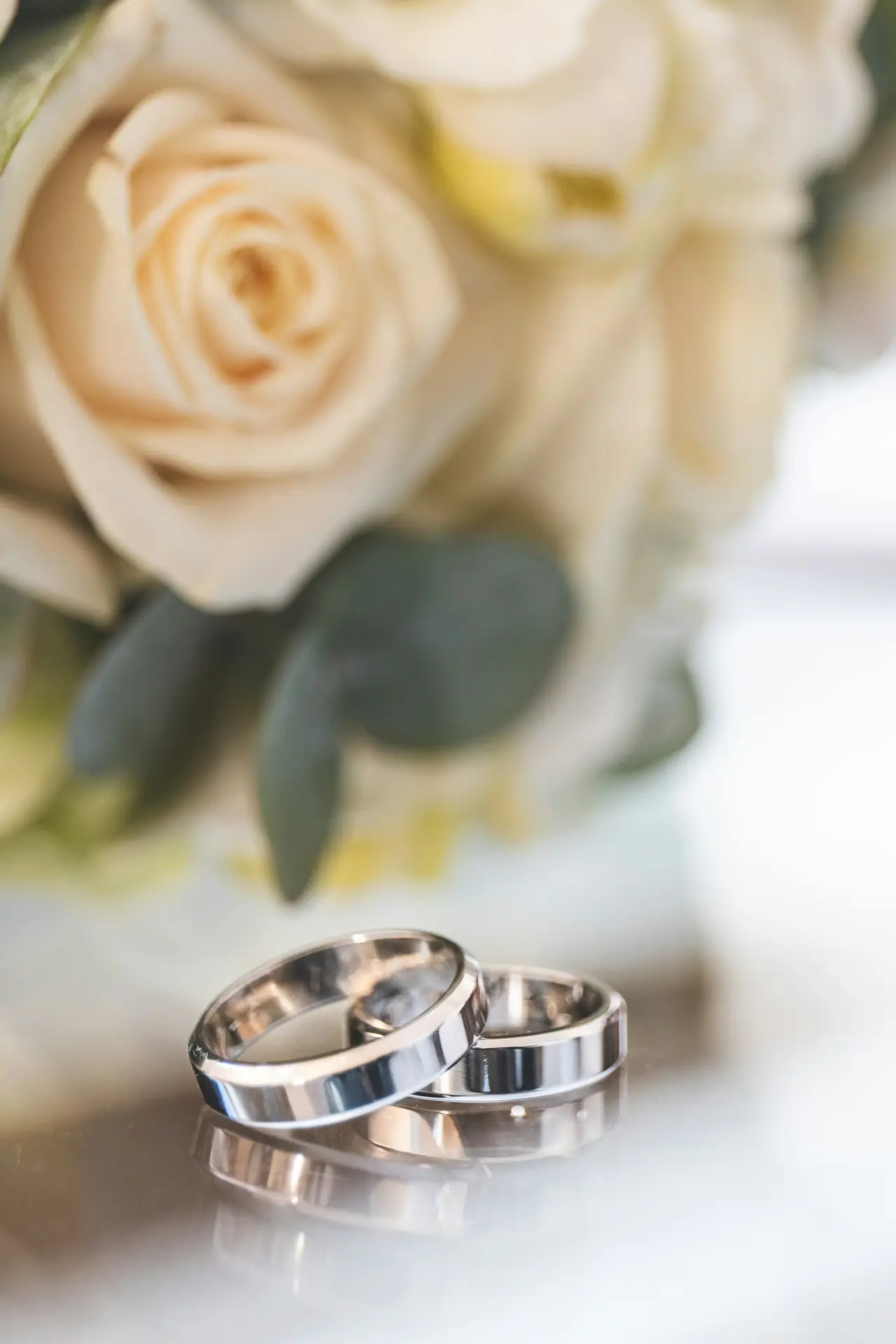 Two wedding rings resting beside cream roses