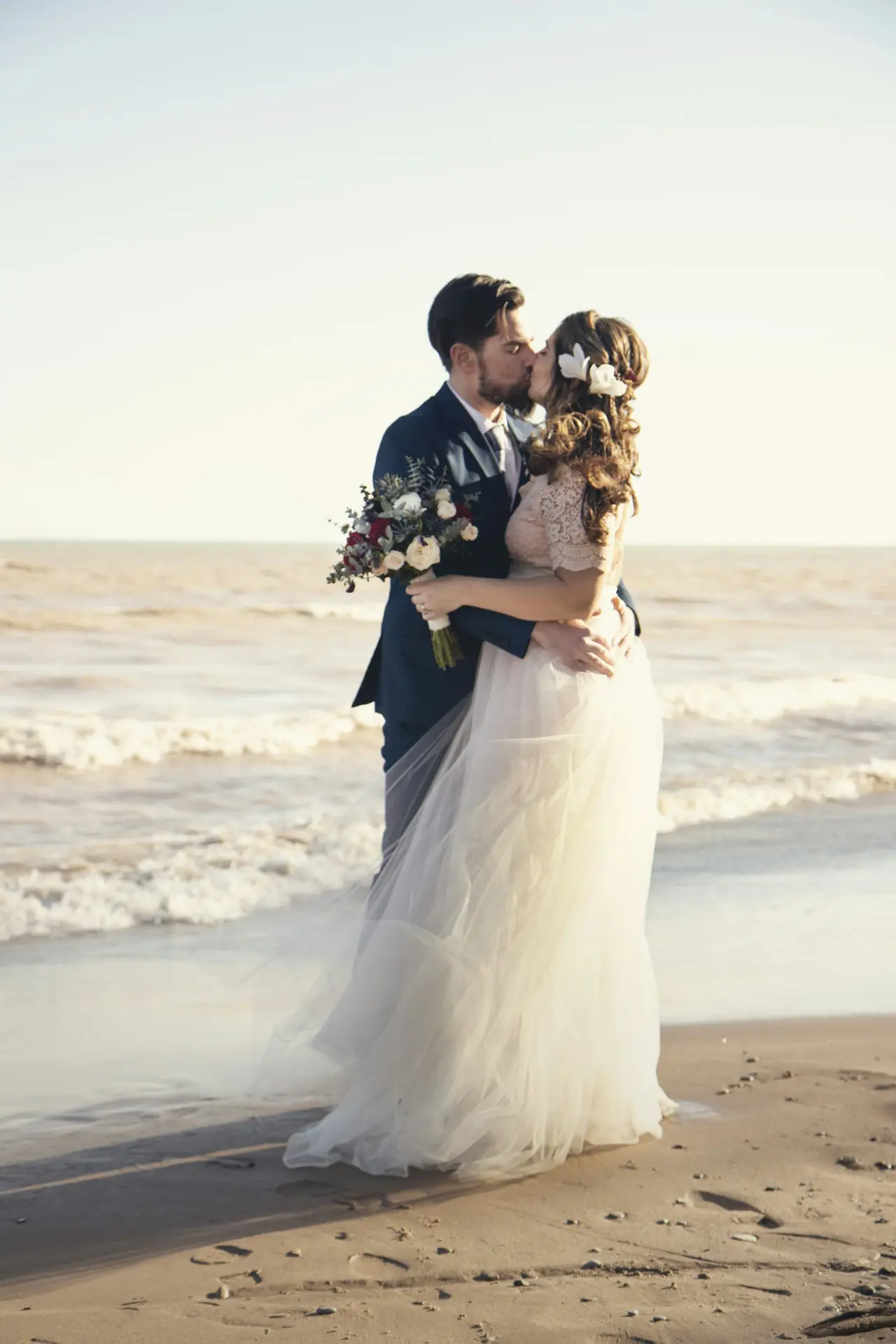 A couple kissing at the water’s edge at sunset