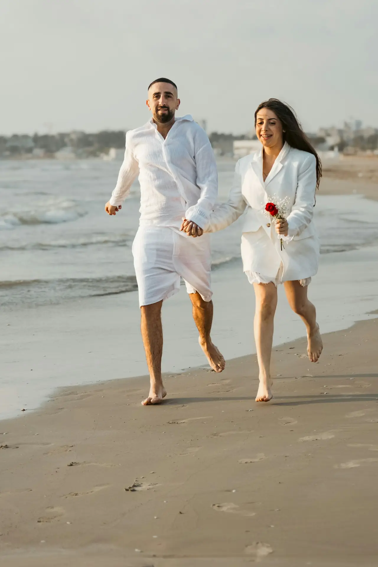 A couple in white running along a wet beach