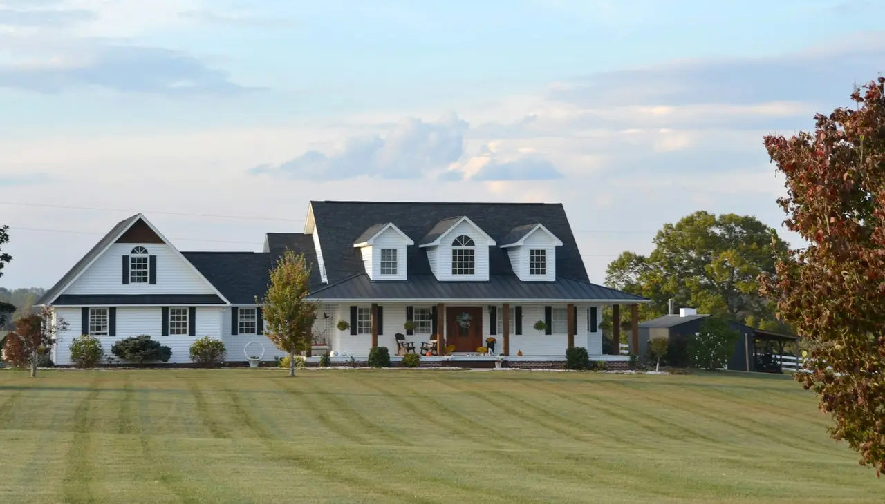A white family home with dormer windows across a big lawn