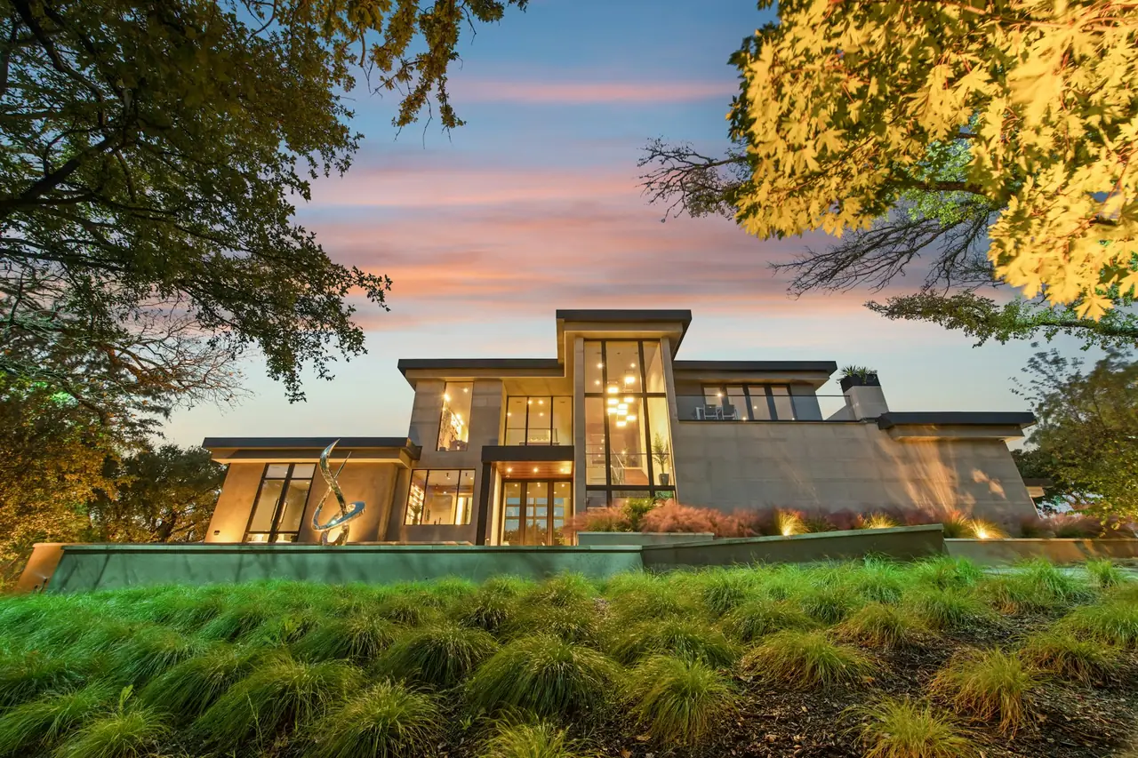 A timber and glass home glowing at dusk behind native grasses