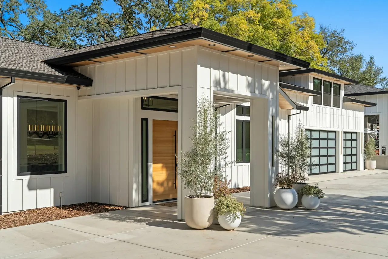 A white two-storey home with timber doors and a wide driveway